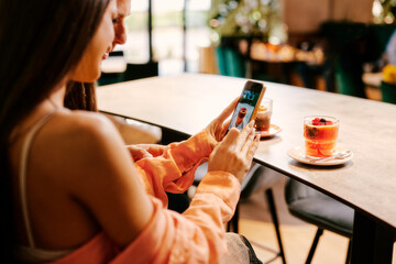 Young women using smartphone to take a photo of smoothie during a date with a handsome young man in a cafe. Selective focus on smartphone display.