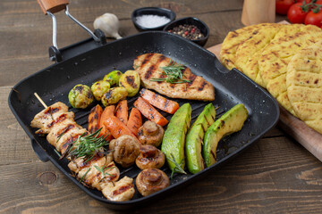 Grilled chicken steakand souvlaki in different variations with avocado, carrot, mushroom and brussels sprout on a teflon pan.