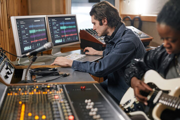 Side view at male musician at audio workstation in professional recording studio, copy space