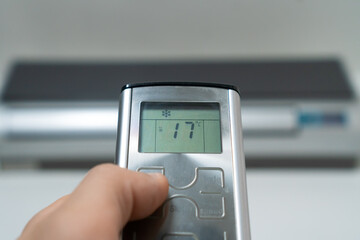 Close-up of a man's hand with a gray remote control pointing at the air conditioner