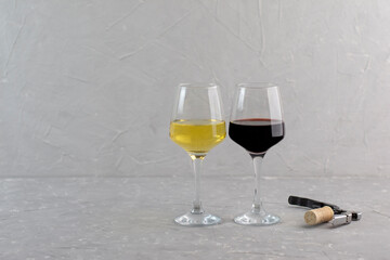 Wineglasses of red and white wine standing side by side in the corner over grey background with copy space