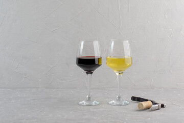 Wineglasses of red and white wine standing side by side in the corner over grey background with copy space