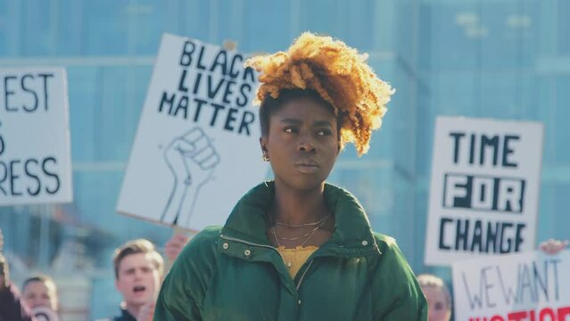 Portrait of female protestor surrounded by marchers holding placards and chanting slogans on demonstration march to promote awareness of black lives matter and racial equality - shot in slow motion