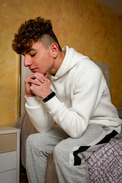 Caucasian Young Man With Curly Hair Sitting On His Bed With A Worried Gesture, He Analyzes The Problems That The Step Of Becoming An Adult Man Entails.