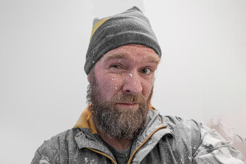 Person all covered in white wall paint. Drops of white paint over the face and beard of a young male man, isolated on white. Painter covered in paint.