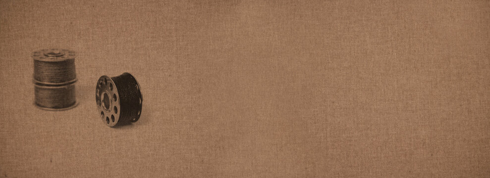 Metal thread spools over a canvas-like background of a coarse woven hard fabric