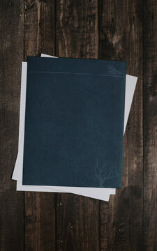 Dark marine colored paper sheet over a stack of white sheets laying on wooden desk made of old dark wood boards
