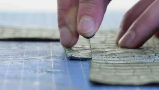 A male tailor cuts artificial leather close-up. Craftsman carving leather at work table, making handicrafts from natural animal skin.