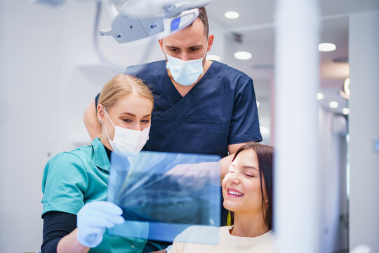 Two dentists examine and repair the patient's teeth. They use X-ray image. Three people in the dental office.