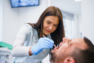 Young white man sitting in medical chair while dentist fixing her teeth at dental clinic.