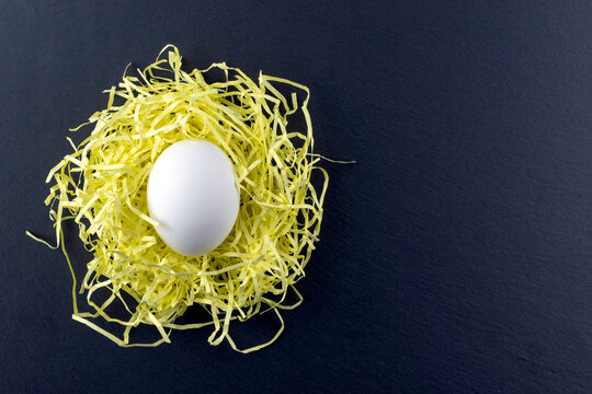 White Easter eggs in a yellow nest on a black background.Funny eggs. Postcard with space for text .