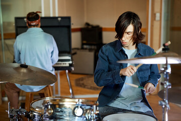 Portrait of young male drummer playing music with band in professional recording studio, copy space