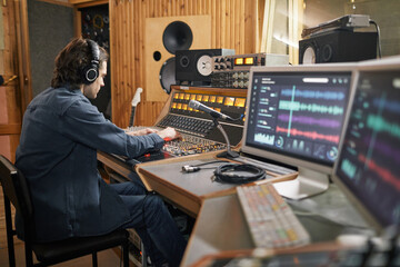 Wide angle at music producer operating audio workstation in professional recording studio, copy...
