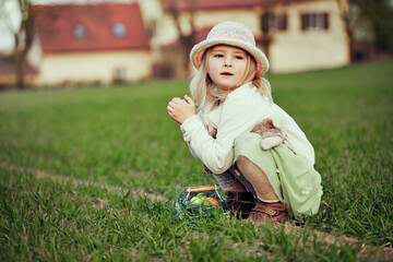 Little girl collecting dyed eggs on Easter egg hunt, on country farm, outdoor