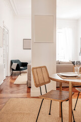 Decorative details of a dining room with a solid wood table with braided wicker chairs and access to a living room with armchairs and lots of light