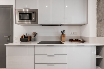 Open kitchen with gray wooden furniture combined with white stone countertop and small appliances on the countertop, cabinets, ceramic hob and microwave oven