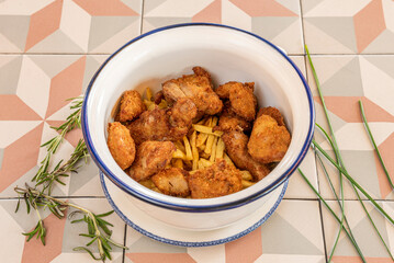 Fried chicken pieces with potatoes and rosemary in a deep enamel bowl