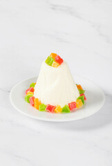 Cottage cheese creamy white chocolate dessert, decorated with colorful candied fruits, on a plate. White background. Bright Easter Holiday