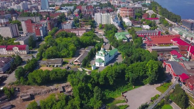 Aerial view of a summer city district with a church and houses. Clip. Beautiful green city located by the long river.