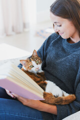 Happiness is a fluffy cat and a great book. Shot of a young woman reading a book with a cat on her lap at home.
