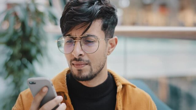 Portrait worried annoyed young arab man standing indoors talking on telephone answering call using smartphone guy angry bad cell service mobile connection problem low battery broken phone microphone