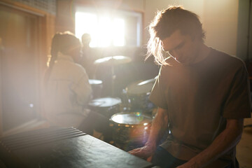 Moody portrait of long haired young man playing music rehearsing with band in dim sunlight, copy...