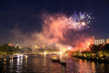 Naklejka na ściany i meble Fireworks explode over boats and crowds enjoying river festival at night