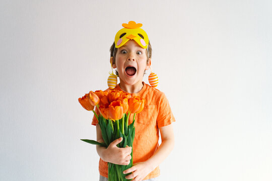 Funny boy with orange tulips and in the mask of a chick on white background. Children celebrating Easter. Happy easter card