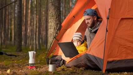 Father and son relaxing together in nature in the spring forest, sitting in an orange tent and...
