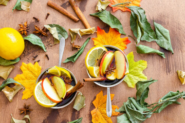 hot mulled wine cooked in two pots with spices, orange and apple on a wooden table with autumn...