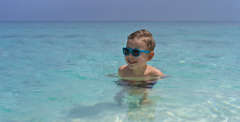 Happy child in sunglasses swims in the Indian Ocean in Maldives