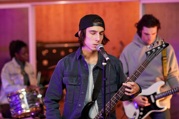 Waist up portrait of talented young man singing with eyes closed in colored studio lights, copy...