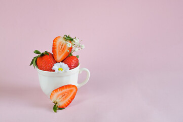 Strawberries in a small white mug with flowers on a pink background with copy space. Daylight