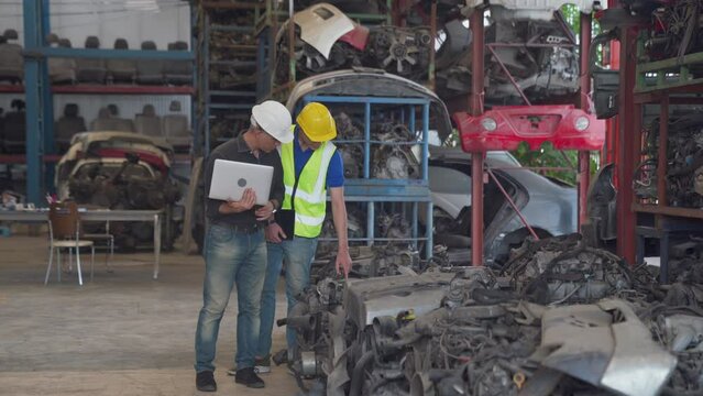 Team of workers and engineer. Worker holding tablet and checking list inventory of old engine in garage. Two man standing at the automotive engine part in the factory.