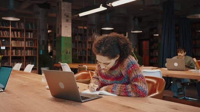 Mixed race female studying remotely using laptop at modern library