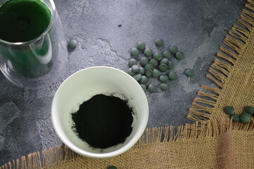 A bowl of green seaweed powder, pills and capsules. 