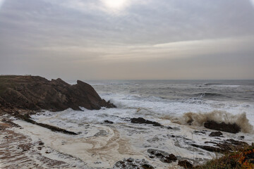 Fototapeta na wymiar Wild Sea in Portugal near Nazare with Foamy Waves Crashing against Rocky Cliffs