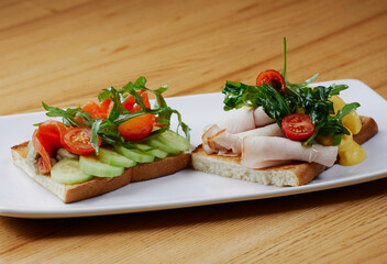 two sandwiches with salmon and avocado, ham and cheese and tomatoes