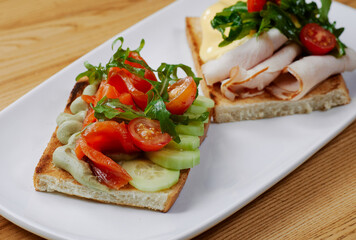 two sandwiches with salmon and avocado, ham and cheese and tomatoes