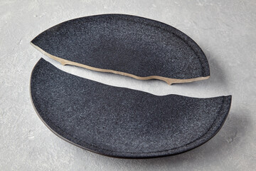 Two halves of a broken dark ceramic plate on a light gray concrete table