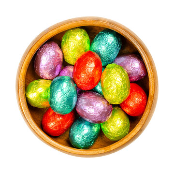 Mixed colored foil wrapped chocolate Easter Eggs, in a wooden bowl. Mini chocolate eggs, sweet candy, wrapped in aluminium foil of different colors. Isolated from above, over white, macro food photo.