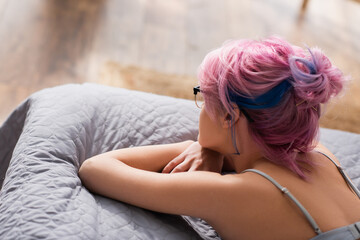 high angle view of young woman with dyed hair lying on bed.