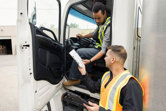 Truck driver and colleague checking schedule on clipboard