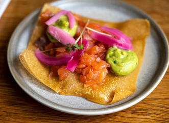 Mexican food, fried corn tortilla with smoked salmon, guacamole sauce and pink pickled onions