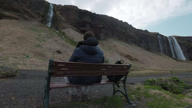 Man sitting on bench near Seljalandsfoss Waterfall In Southern Iceland. incredible waterfall in Iceland, tourist enjoying amazing view of Iceland nature. Wide angle shot, high quality 4k footage