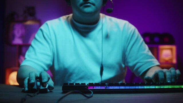 Gamer playing computer game, streamer wearing headphones. Young man playing video games using backlight keyboard. Programmer or hacker working in networks, cyberspace.
