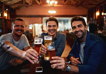 Wish you were here. Portrait of a group of young friends seated at a table together while enjoying a beer and celebrating with a celebratory toast inside a bar.