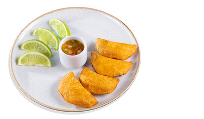 Colombian empanadas with spicy sauce and lemon wedges on a plate, top view