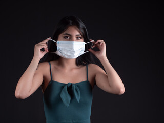 Hispanic woman putting on surgical mask isolated on black background