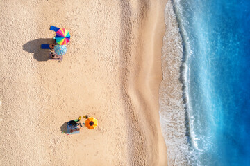 Aerial view of blue sea, waves, sandy beach and umbrellas with lying people at sunset in summer. Tropical landscape with clear turquoise water. Top view from drone. Lefkada island, Greece. Travel - obrazy, fototapety, plakaty